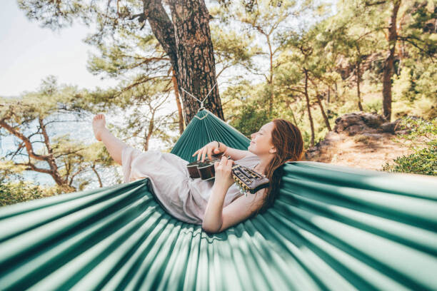 Levně Plakát, Obraz - Woman relaxing in hammock and playing, Maria Korneeva, 40 × 26.7 cm
