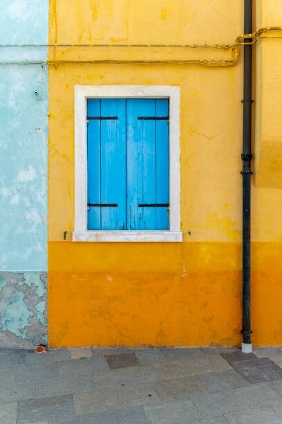 Levně Plakát, Obraz - Yellow house with blue window, colorful, imageBROKER/Moritz Wolf, 26.7 × 40 cm
