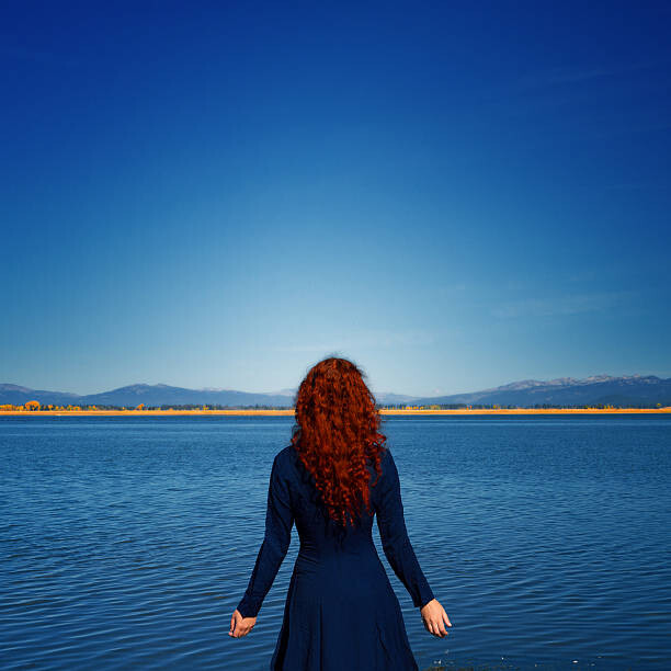 Umělecká fotografie Redhead in blue dress faces rippled lake, Anna Gorin, (40 x 40 cm)