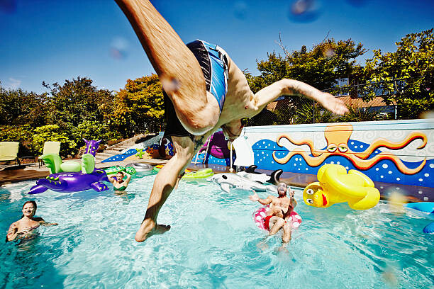 Umělecká fotografie Man in mid air jumping into pool during party, Thomas Barwick, (40 x 26.7 cm)