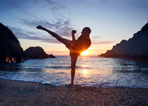 Fotografie de artă Man practising kung fu kick along beach at sunset