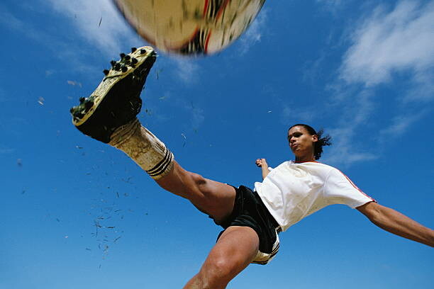 Photographie artistique Soccer player kicking ball, low angle