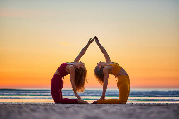 Umelecká fotografie Two women doing yoga on the beach at sunrise