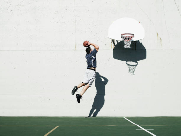 Fototapeta Man dunking basketball on outdoor court,