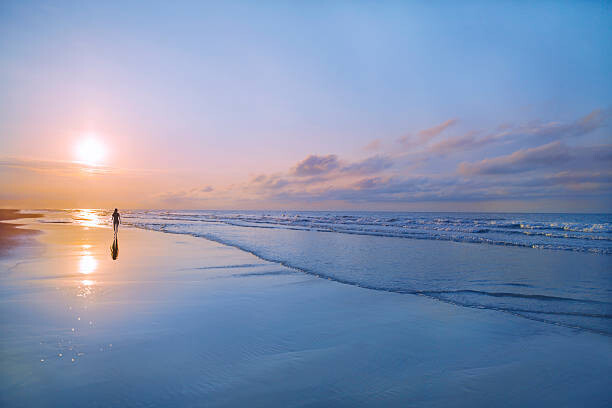 Fototapeta Person walking on beach at sunrise