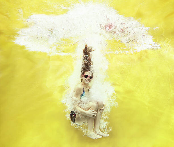 Obraz na plátně Girl jumping into water on yellow background
