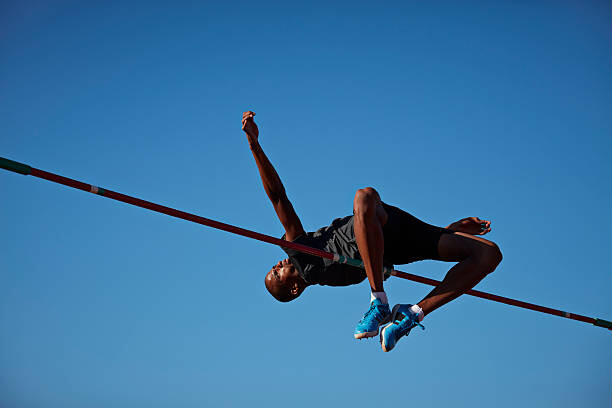 Obraz na plátně Male athlete doing high jump at sunset