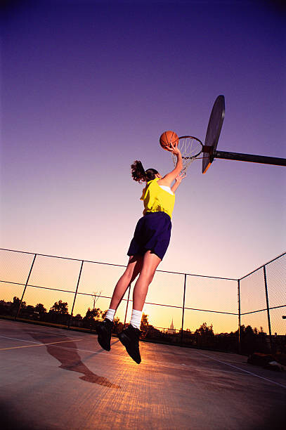 Obraz na plátně Young woman dunking basketball in net,