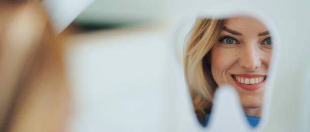 Plagát Happy patient looking at her teeth in mirror.