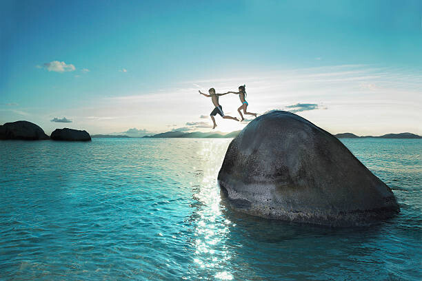 Plakat Two kids holding hands jumping off rock into sea