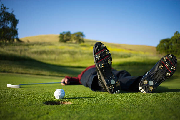 Plakát Golfer lying on green, ball on edge of hole