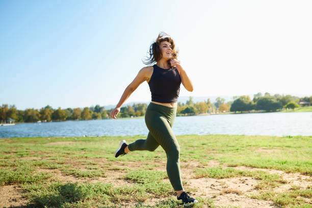 Plakát Smiling young woman jogging near lake on sunny day
