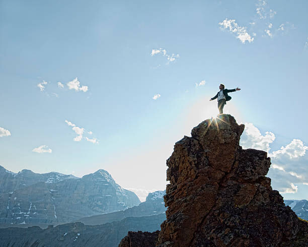 Poster Man stands on peak, arms outstretched.