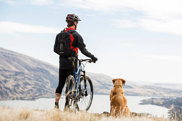 Póster A man mountian biking with his dog.