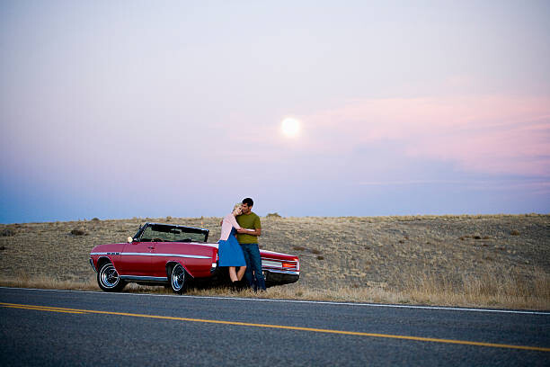 Tableau sur toile man and woman next to a red convertible