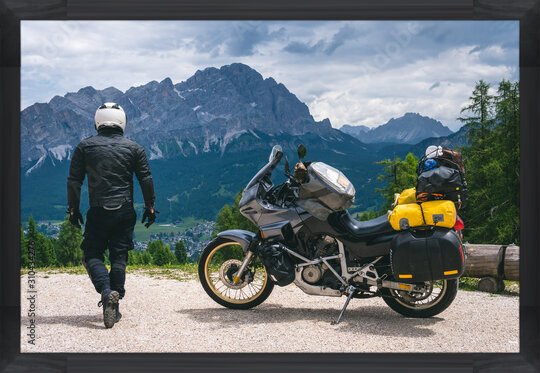 Photos Back view of biker with adventure touring motorcycle in full equipment on dirt road, High top mountains on background, tourism travel concept, copy space